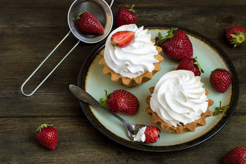 Sweet dessert. Round cakes with airy protein cream and fresh ripe strawberries on an old dish on a wooden table. 