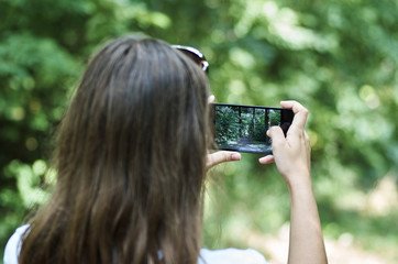 A young girl by mobile phone is photographing a landscape with a forest