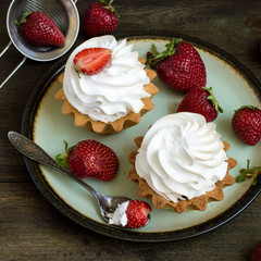 Sweet dessert. Round cakes with airy protein cream and fresh ripe strawberries on an old dish on a wooden table. 