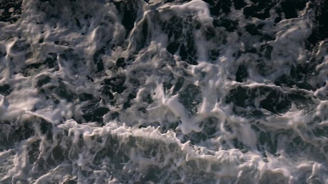 Slow motion disturbed ocean water surface by sailing boat at sunset.