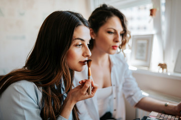 Two women doing makeup indoors in apartment.