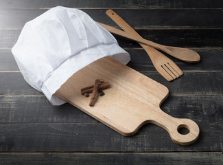 Chef hat,empty cutting board and spoons on black wood