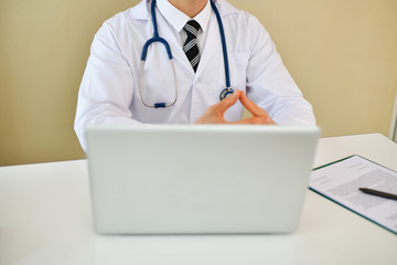 Smiling doctor posing in the office, he is wearing a stethoscope, medical staff on the hospital background