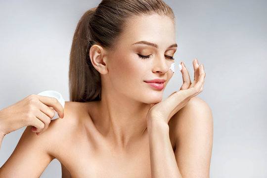 Attractive woman applying moisturizing cream on grey background. Beauty & Skin care concept
