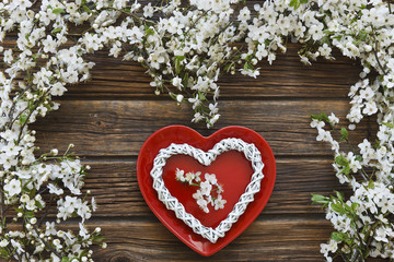 Close-up photo of Beautiful white Flowering Cherry Tree branches with red dish heart shape. Wedding, engagement or betrothal concept on vintage wooden background. Top view, greating card.