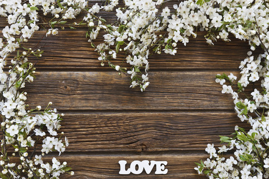 Close-up photo of Beautiful white Flowering Cherry Tree branches with  white letters love. Wedding, engagement or betrothal concept on vintage wooden background. Top view, greating card.