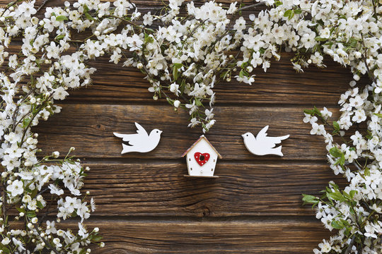 Close-up photo of Beautiful white Flowering Cherry Tree branches with two wooden birds and birdhouse. Wedding, engagement or betrothal concept on vintage wooden background. Top view, greating card.