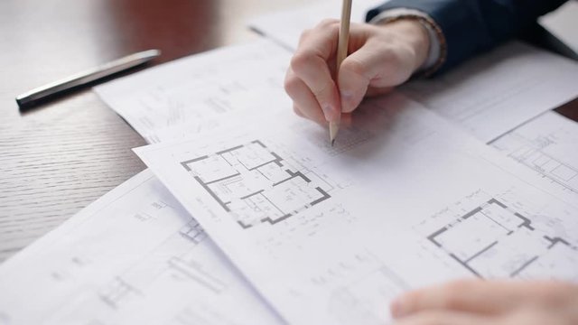 Close up hands of male architect correcting house blueprint. Concept of: architecture modern, house building, blueprint drawing, engineering people, paper work.
