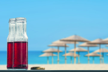 Pomegranate cold juice in bottles on the beach and straw umbrellas backgrounds 
