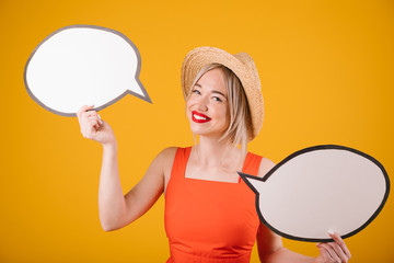Summer time mood blonde woman in straw hat and red fancy dress is holding speech buble banners. Yellow background. empty space