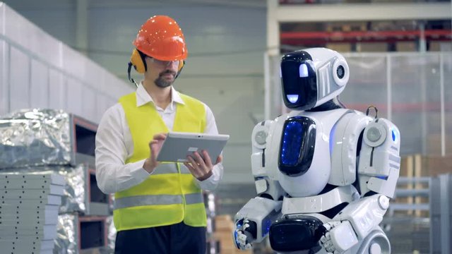 Factory employee is communicating with a humanoid in gestures