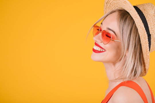 Smiling beautiful blonde woman in starw hat on cheerful yellow background. Heart shaped pink sunglasses. Summer love