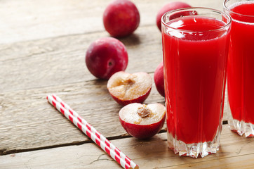 Plum juice in glass glasses with plums and straws for juice on wooden table