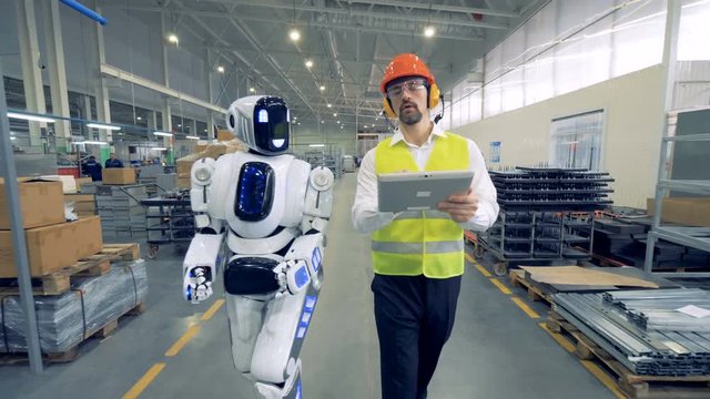 Human factory worker and a robot are walking together in factory premises