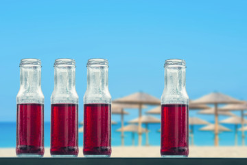 Pomegranate cold juice in bottles on the beach and straw umbrellas backgrounds 