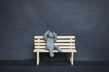 Sad plasticine man on a wooden bench on the dark background.