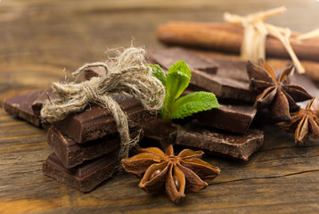 Pieces of chocolate, cinnamon and star anise on a wooden table.