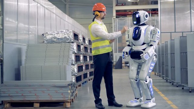 Factory employee and a humanoid are communicating in a factory facility.