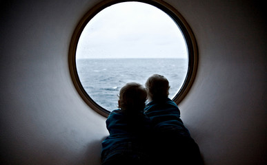 Two children are looking through the porthole, the ferry, the autumn, the Baltic Sea