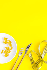 Dietary supplement for well-being. Fish oil or omega-3 capsules on plate near measuring tape on yellow background top view copy space