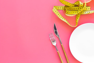Diet for weight loss concept. Proper nutrition. Medical starvation. Empty plate with fork and knife near measuring tape on pinkbackground top viewspace for text