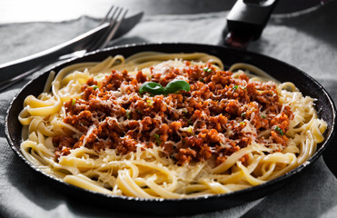 Traditional pasta spaghetti bolognese in a frying pan on dark wooden background