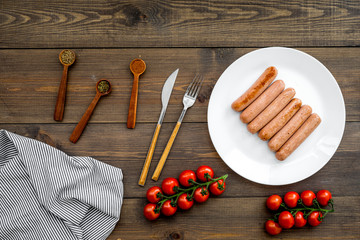 Grilled sausages on dark wooden table near cherry tomatoes and spices in wooden spoons top view