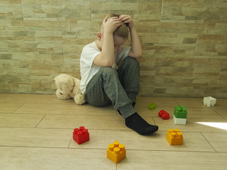 little sad boy sits on the floor with a block, teddy bear toy
