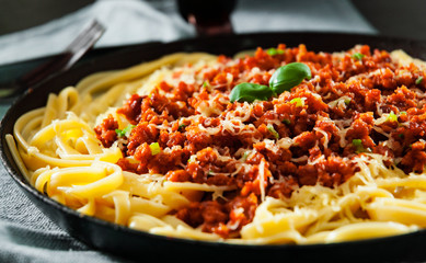 Traditional pasta spaghetti bolognese in a frying pan on dark wooden background