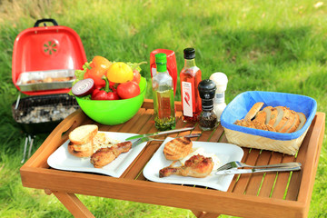 Tacę ogrodową z grilowanym jedzeniem, warzywami i pieczywem i grilem w tle. © Stanisław Błachowicz