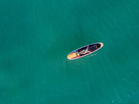 Nondescript fit female in a bikini lounging on her SUP Stand Up Paddle Board in the ocean from a birds eye view