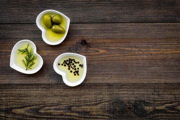 Olive oil as healthy diet product. Heart shaped bowls with olive oil with green olives, rosemary and black pepper inside on dark wooden background top view copy space