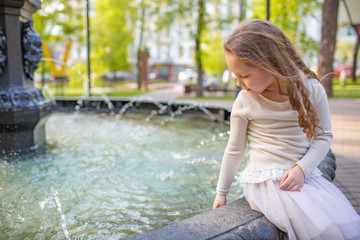 Cute little girl playing by city fountain on hot and sunny summer day. Child having fun with water in summer. Active leisure for kids.