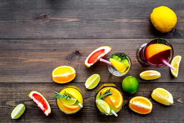 Tropical fruit cocktail with alcohol. Glass with beverage near oranges, grapefruit, lime and rosemary on dark wooden background top view space for text