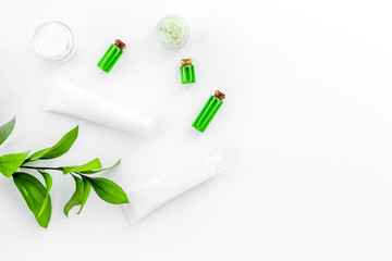 Natural cosmetics for skin care near green leaves on white background top view copy space