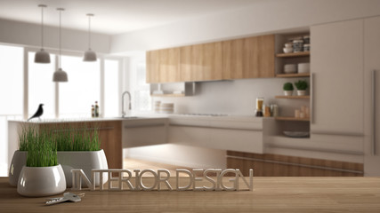 Wooden table or shelf with potted grass plant, house keys and 3D letters making the words interior design, over blurred modern kitchen, project concept architecture background