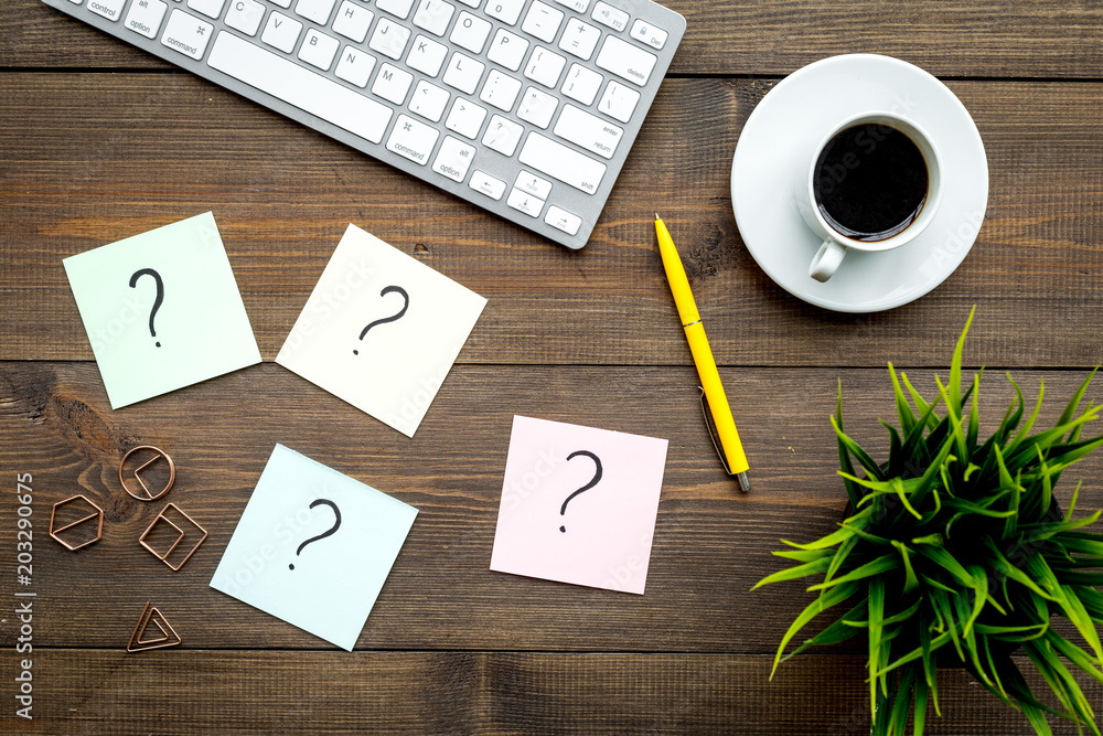 Poster question mark on sticky notes on office desk on dark wooden background top view. faq concept. workin