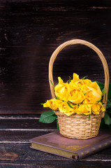Fototapeta na wymiar Yellow roses in a basket, vintage book on wooden background. Free space for your text