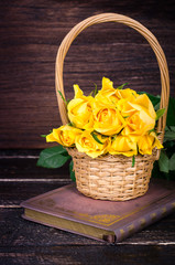 Fototapeta na wymiar Yellow roses in a basket, vintage book on wooden background. Free space for your text