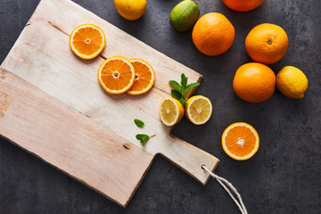 Flat lay of fresh citrus fruits, half cut orange and lemons on cutting board on black stone background. Copy space. Horizontal top view.