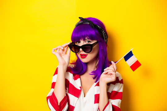Young surprised girl with purple hair holding french flag on yellow background.