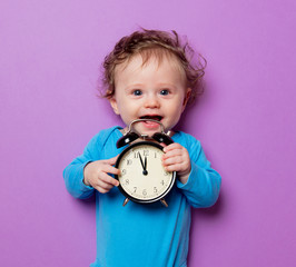little infant baby with alarm clock lying on purple background
