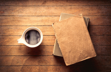 White cup with coffee and books on wooden table. High angle view