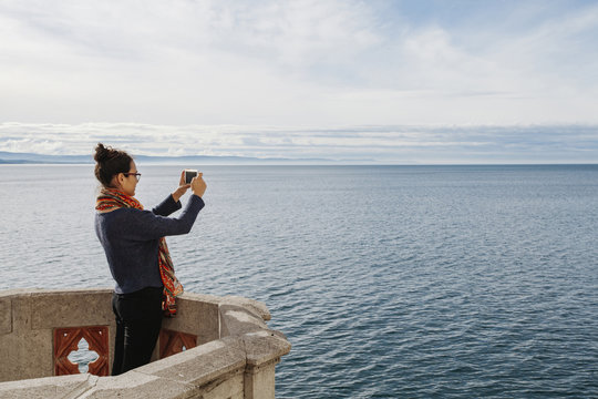 Woman photographing sea with smartphone while standing on terrace