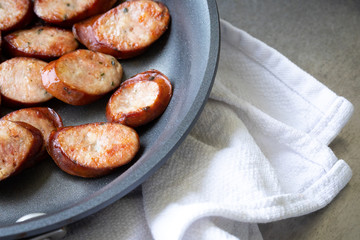 Sliced sausages in a nonstick pan cooling on a towel, with space for text on right
