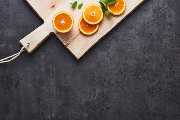 Flat lay of fresh citrus fruits, half cut orange slices on cutting board on black stone background. Horizontal top view with copy space.