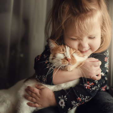 A small cute child with naked hair gently embraces a red fluffy cat