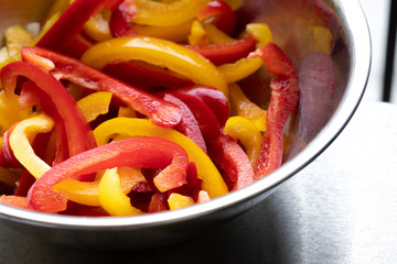 Sliced red and yellow bell peppers in a metal cooking bowl
