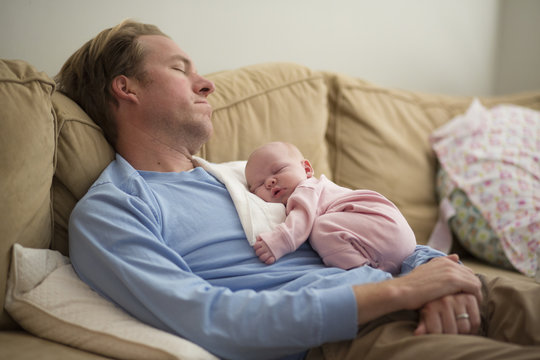 Father with baby girl sleeping on sofa at home