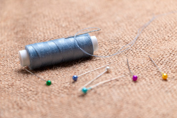Coil thread with a needle stuck in it next to the tailor pins on the burlap